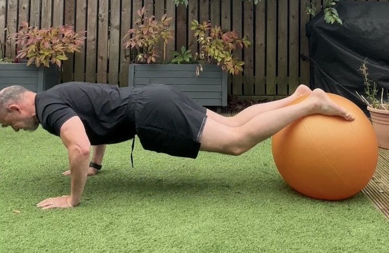 Stephen halfway down a press-up with hands on the floor and feet on a Swiss ball