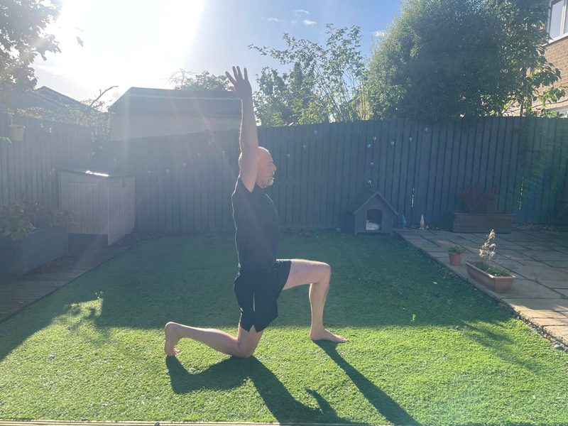 Stephen kneeling in a hip flexor stretch, side view, back knee on the ground and one arm reaching overhead