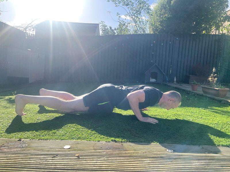 Stephen at the bottom of a press-up, side view, chest just above the ground and body in a straight line