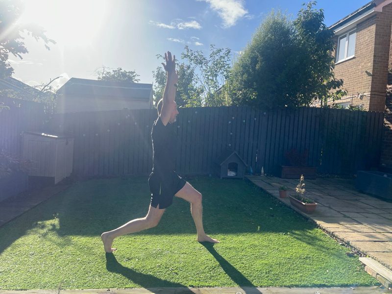 Stephen at the top of a split squat, side view, one foot forward, one arm raised